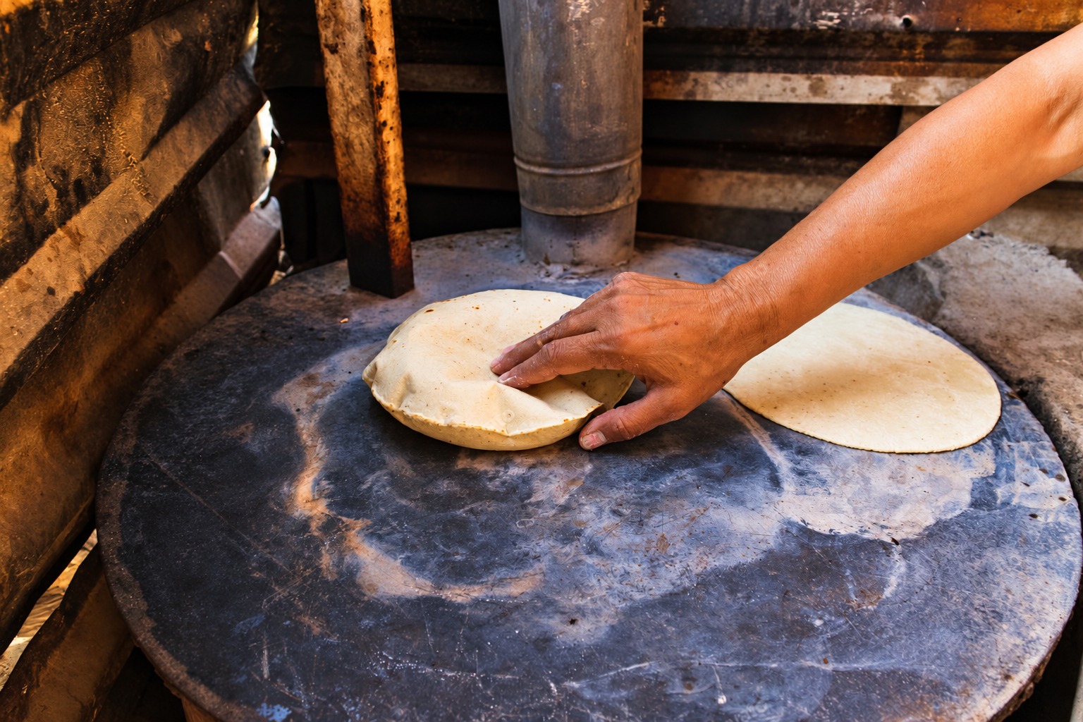 A hand tending to a puffed roti on a traditional cooking surface